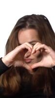 Woman is portraying heart by her hands before her face on a white background in the studio. Close-up Vertical video