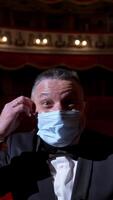Happy actor puts off medical mask and throws it. Man in costume sitting in the empty theatrical hall and invites joyfully to come to performance. The end of pandemic. Vertical video