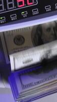 Electronic operations for counting paper money. Cash money counting machine. Banknote counter are counting one hundred dollar bills. Top view. Close-up. Vertical video
