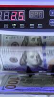 Money counting equipment for paper money calculation. Automatic mechanism for bank financial operations. Currency exchange of one hundred dollars. Close-up. Vertical video