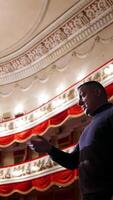 Man is giving interview in the opera house. Middle-aged actor talking to someone while standing on stage on classical theatre background. Vertical video