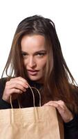 A beautiful woman in a black sweater looks mysteriously in a paper packbag and throws it in frustration and go away on the white background. Purchases. Shopping Vertical video