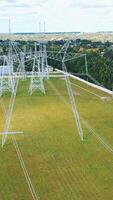 Electricity pylons in the countryside. Power station with white tall towers on field. Distribution of electricity. Motion camera back. Vertical video