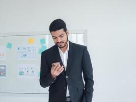 Business man portrait Asian one person wearing a black suit, handsome cool sharp smart standing looking, hand holding mobile phone and tablet ready for work inside the office, with white background photo