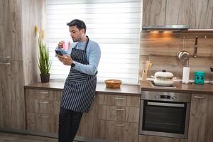 Man in the kitchen using mobile phone while waiting for meal to cook photo