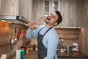 Man holds a spatula in his apron and sings in the kitchen photo