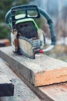An old working chainsaw is lying on a sawn board fifty millimeters. Photos on the street in the yard for ideas for building from wood and planks. High quality photo
