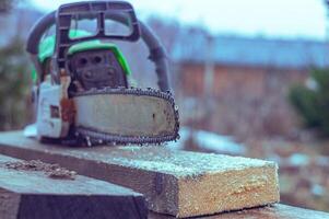 An old working chainsaw is lying on a sawn board fifty millimeters. Photos on the street in the yard for ideas for building from wood and planks. High quality photo