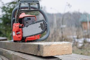 An old working chainsaw is lying on a sawn board fifty millimeters. Photos on the street in the yard for ideas for building from wood and planks. High quality photo
