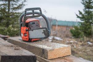 An old working chainsaw is lying on a sawn board fifty millimeters. Photos on the street in the yard for ideas for building from wood and planks. High quality photo