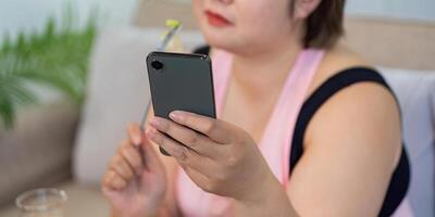 Overweight woman using smartphone while enjoying a healthy meal at home, focusing on weight loss. photo