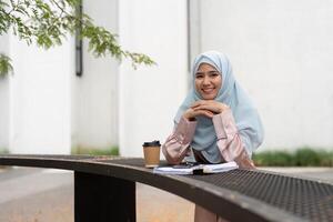 Muslim businesswoman smiling with coffee and documents at outdoor table. photo