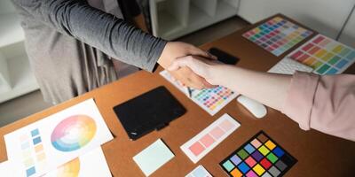 Close-up of graphic designers shaking hands over a desk with color palettes. photo