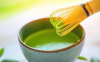Fresh green matcha tea being whisked in ceramic bowl, creating vibrant and smooth texture. whisk adds touch of elegance to preparation process photo
