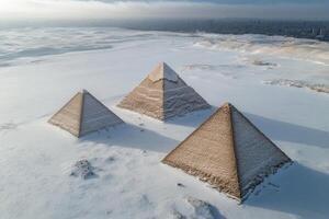 Three iconic pyramids rise above a blanket of snow, surrounded by vast desert expanse. Clouds loom overhead, creating a mystical atmosphere in this extraordinary view. photo