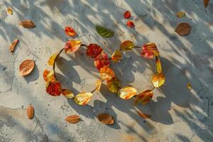 A circular arrangement of vibrant autumn leaves rests on a concrete surface, illuminated by soft late afternoon sunlight, with scattered leaves around photo
