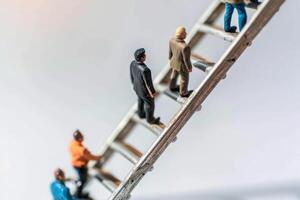 Miniature figurines ascend a silver ladder, representing the journey of climbing towards success and the challenges of personal and professional development photo