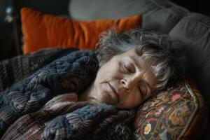 The elderly woman sleeps soundly on the couch, wrapped in a warm blanket. Sunlight softly illuminates her serene expression, creating a tranquil atmosphere photo