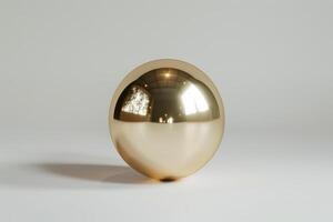 A polished gold sphere sits on a light surface, reflecting natural light and surrounding details, creating an elegant and modern aesthetic within a minimalist environment photo