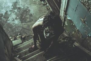 A disturbing figure with a painted face is seen creeping up a grimy set of stairs in a dilapidated building during the twilight hours, evoking a sense of dread photo