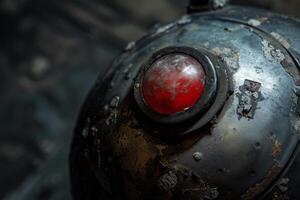 A close-up captures a worn metal sphere featuring a striking red button at its center. The surface reveals rust and age, indicating long-term exposure to the elements and industrial use photo