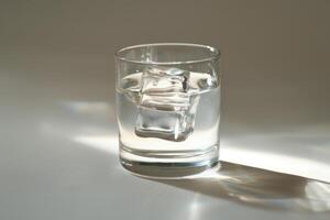 A clear glass holds refreshing water with several ice cubes, gently melting and creating a serene atmosphere in soft afternoon light photo
