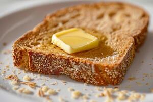 A slice of golden-brown toasted bread rests on a white plate, topped with a melting pat of butter, ideal for a comforting breakfast or snack photo