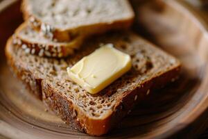 Two slices of whole grain bread sit on a wooden plate, topped with a melting pat of butter, ideal for a delightful breakfast experience photo