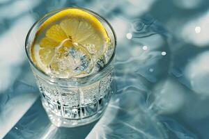 A glass filled with sparkling lemonade, complete with a lemon slice, reflects light. The drink rests on a sunlit, shimmering surface, evoking a refreshing summer vibe photo