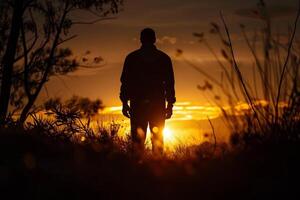A man stands in a field at sunset, silhouetted against the sky photo