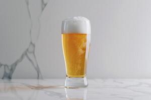 A clear glass filled with golden beer showcases a thick layer of creamy foam at the top, displayed on a sleek marble countertop in bright lighting photo