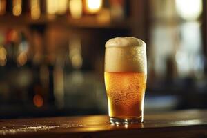 A frothy beer fills a chilled glass, resting on a wooden bar. Soft lighting from the background creates a warm and inviting atmosphere in the pub photo