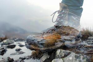A hiker is navigating through rocky trails, their boot splashed with water and dirt, surrounded by a foggy backdrop evoking a sense of adventure in the wilderness photo