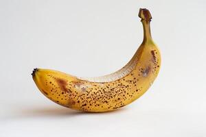 The yellow banana displays a variety of brown spots, indicating its ripeness. It sits upright against a clean white background, highlighting its curves and texture photo