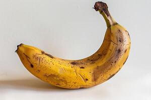 This yellow banana stands upright against a neutral backdrop, displaying its curved shape and speckles. The lighting emphasizes its glossy skin, suggesting ripeness photo