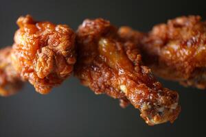 Crispy fried chicken wings are suspended in front of a dark backdrop, showcasing a rich, glossy sauce that enhances their delicious appearance photo
