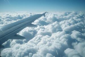The wing of an airplane extends over a sea of fluffy clouds, with bright sunlight illuminating the scene on a clear day. The vast sky showcases a serene backdrop photo