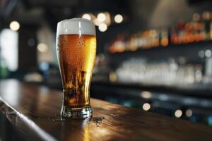 A refreshing glass of golden beer is placed on a polished wooden bar top in a lively pub. The background features soft lighting and blurred shelves filled with drinks photo