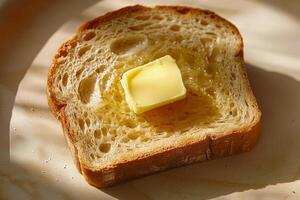 A slice of fresh bread sits on a plate with a square of butter melting on top, illuminated by soft, natural light during breakfast photo