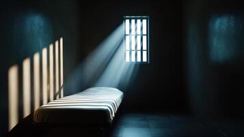 A bed in a dark room with sunlight shining through the bars photo