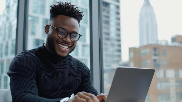 A man wearing glasses is smiling while using an Apple laptop photo