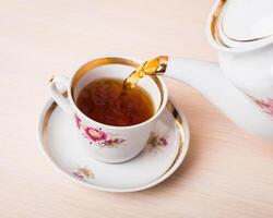 Old-style porcelain kettle pouring tea from jug to cup of tea photo