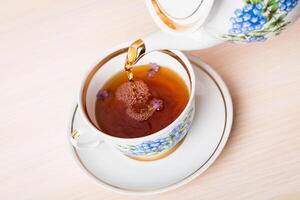 Old-style porcelain kettle pouring tea from jug to cup of tea photo