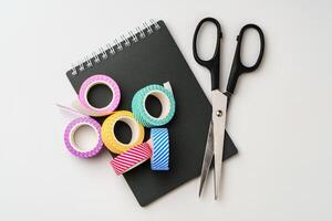 Crafting essentials on a workspace featuring colorful tape and scissors beside a notepad photo