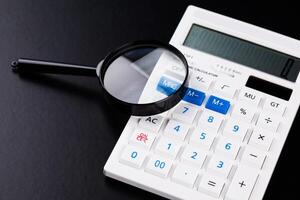 Calculator with a magnifying glass on a black background photo