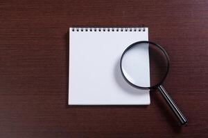 Notebook and magnifier on a wooden background photo