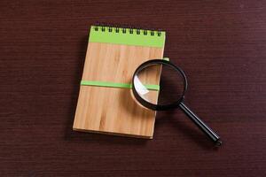 Notebook and magnifier on a wooden background photo
