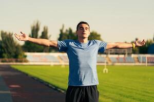 Young man stretches with arms wide open on a track field during sunset, embracing the moment of relaxation photo