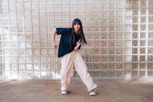 Young dancer performs expressive moves against glass block wall in urban environment during daytime photo