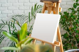 Artist's easel set up with a blank canvas surrounded by indoor plants in a cozy studio environment photo